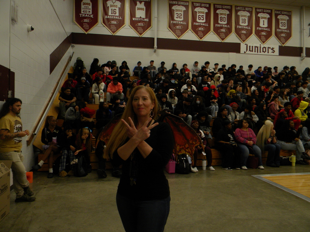 teacher with dragon wings. students on bleachers at pep rally