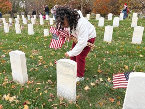 A student places a flag in front of a headstone at a cemetery.