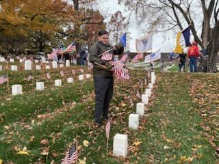 A student places a flag in front of a headstone at a cemetery.