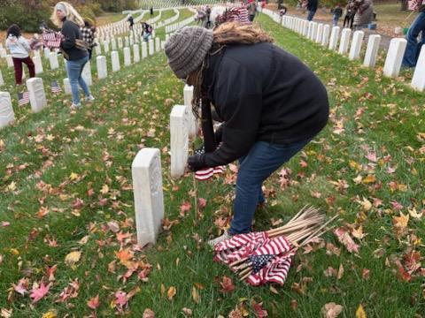 A student places a flag in front of a headstone at a cemetery.