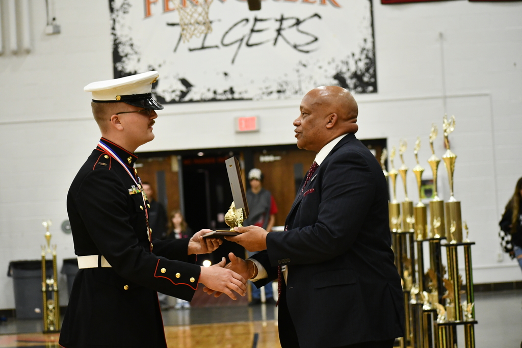 Dr. Brian Yearwood shakes hands with and presents an award to a MCJROTC representative.