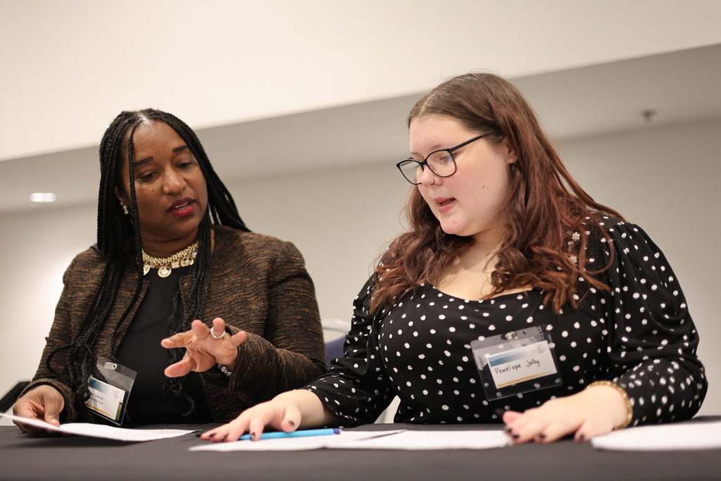 An adult and a student sit at a table and speak.