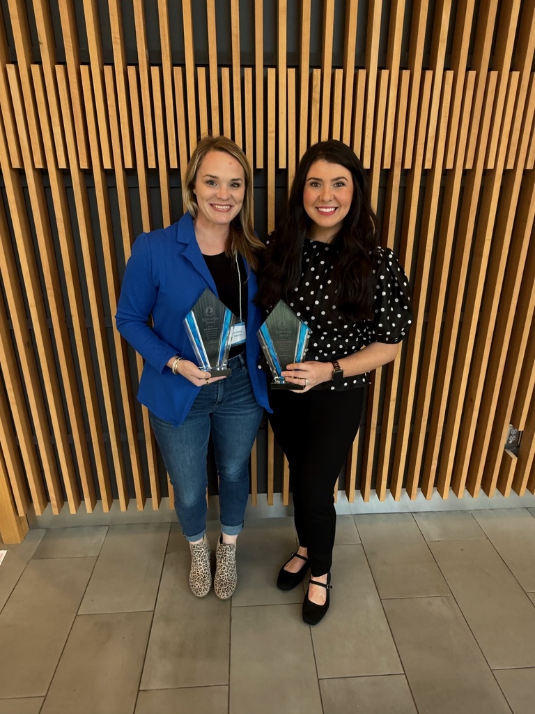 Two women pose for a picture and smile while holding their awards.