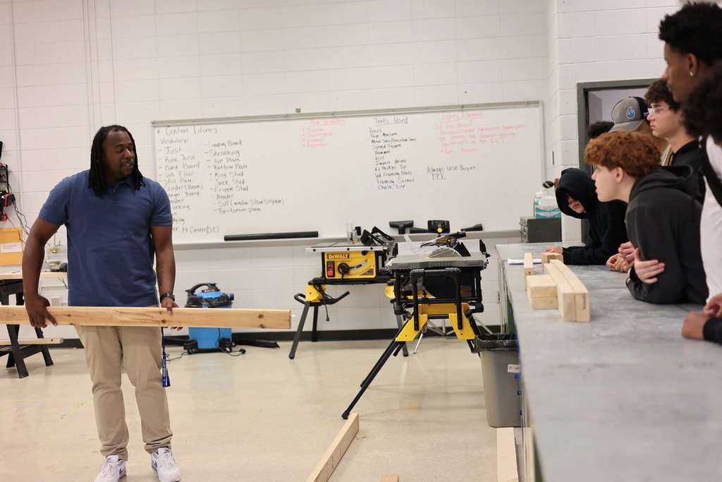 A teachers holds a 2x4 while students watch.