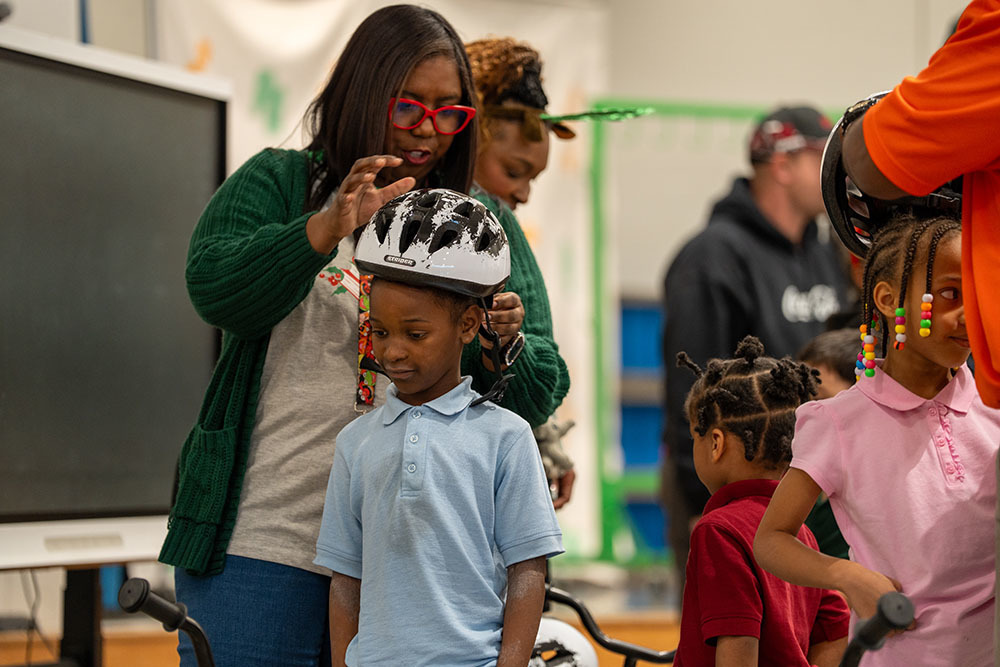 An adult fits a bike helmet on a student's head. 
