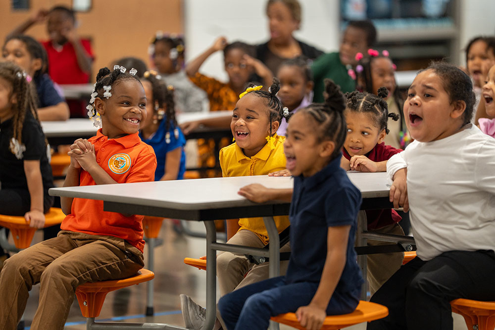 Students smile and cheer while sitting at a table.