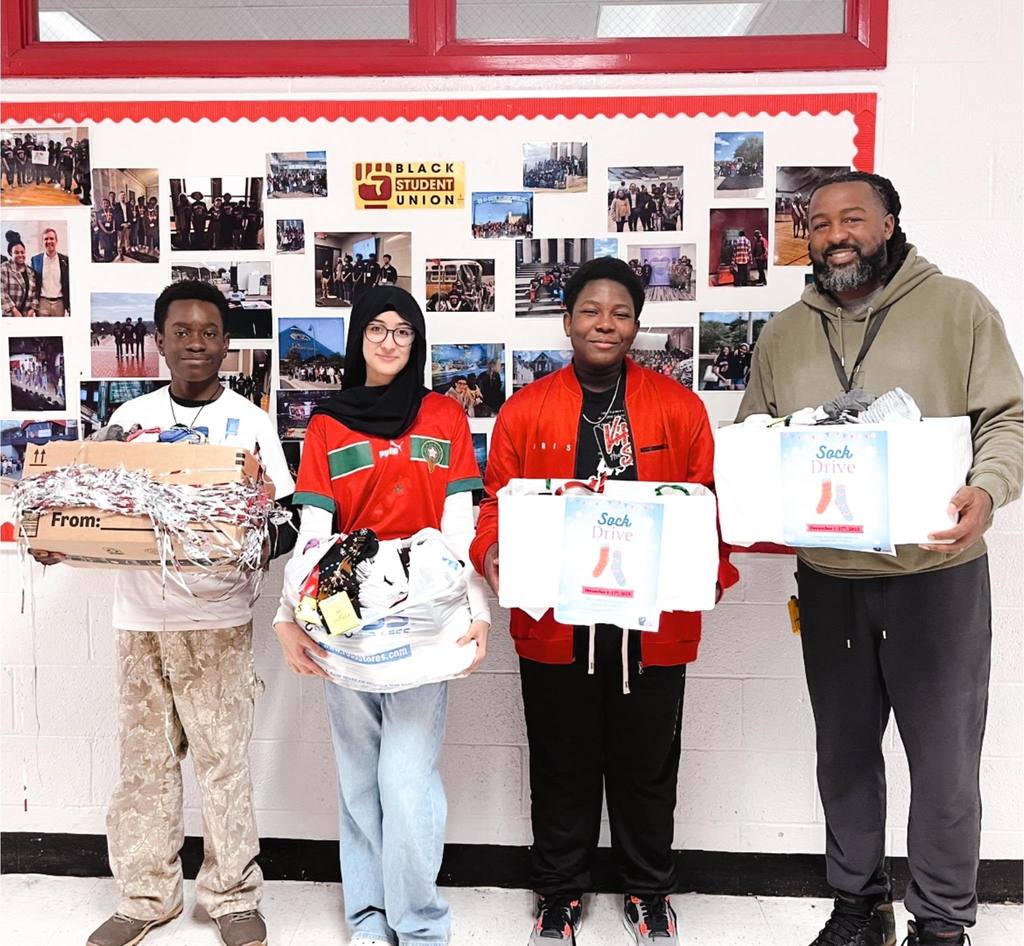 Three students and an adult hold sock donations.