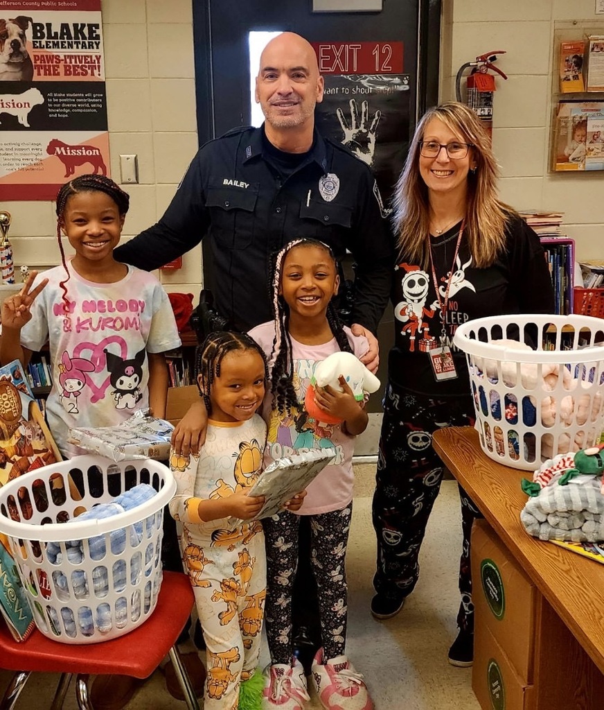 A police officer and an adult pose for a picture with three students who are holding gifts.