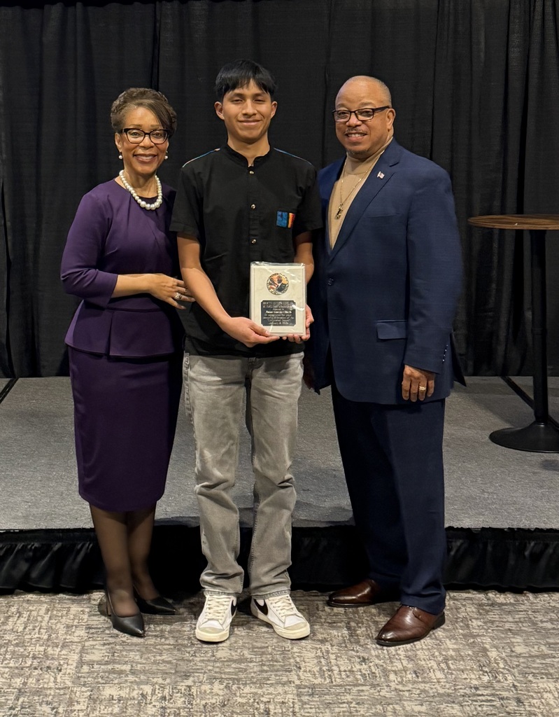 A student holds a plaque and poses for a picture with two adults.