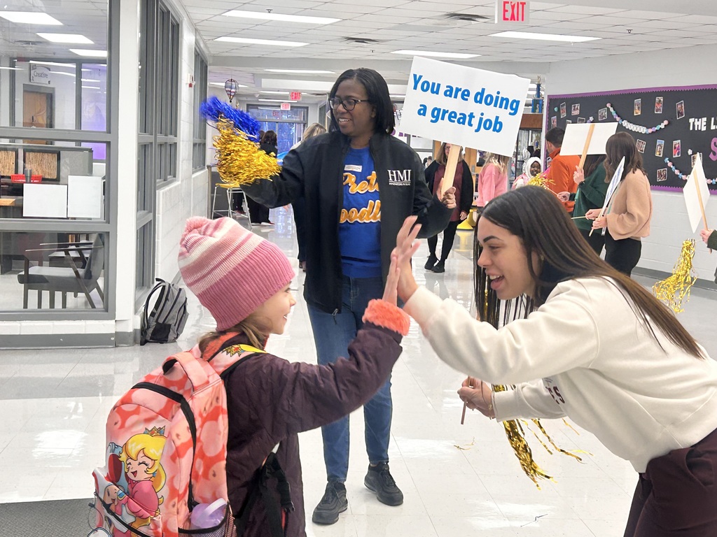 Mornings with Moms volunteers cheer for students as they enter the school building.
