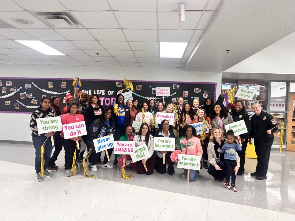 Mornings with Moms volunteers pose for a picture ohlding signs and pom poms.