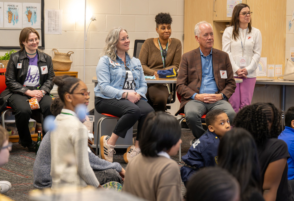 Adults watch as students sit on the classroom carpet. 