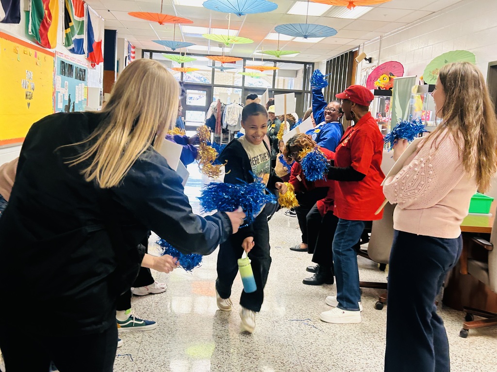 A student walks down the hall as Mornings with Moms volunteers cheer and wave pom poms.