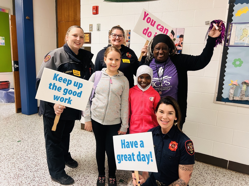 Mornings with Moms volunteers pose for a picture with two students and smile.