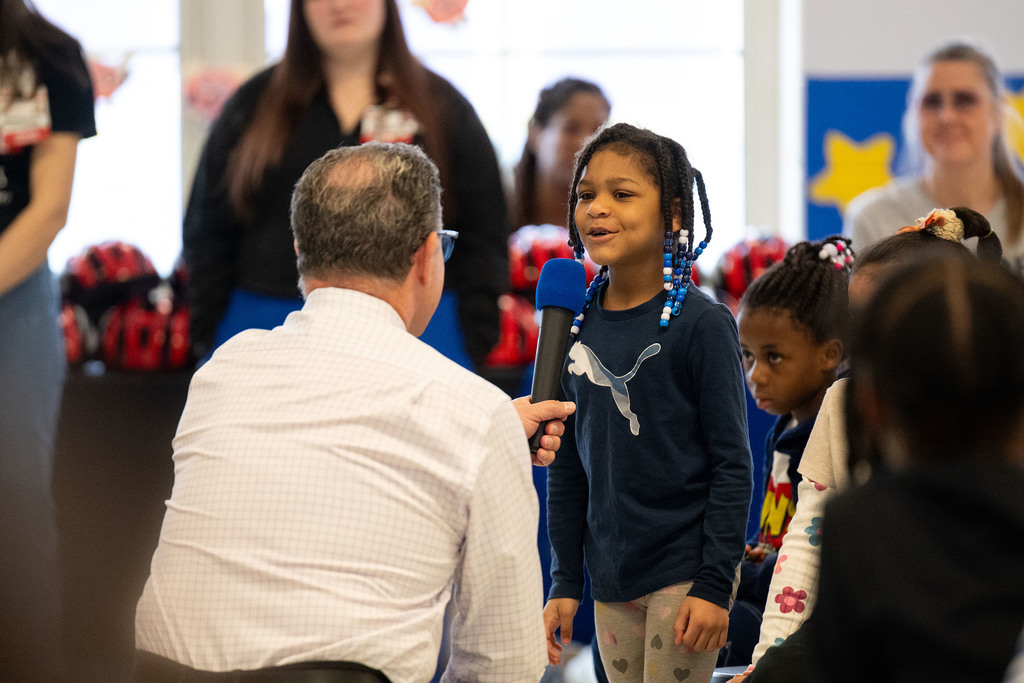 A student speaks into a microphone held by an adult.
