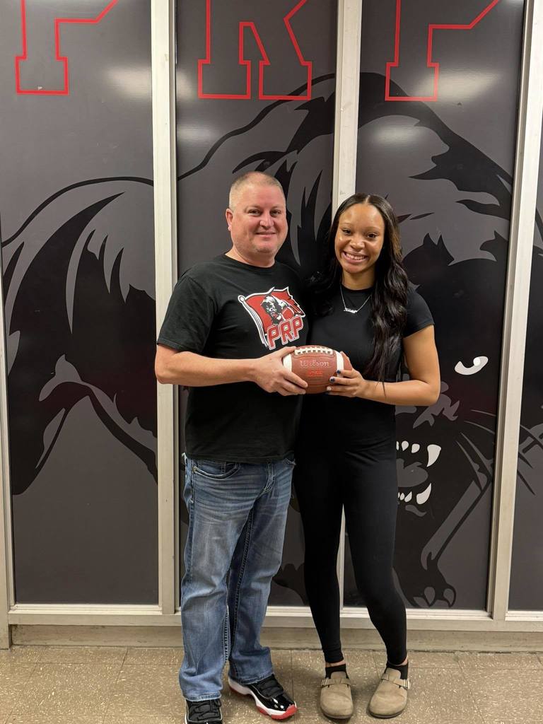 An adult and a student hold a football and pose for a picture while smiling.