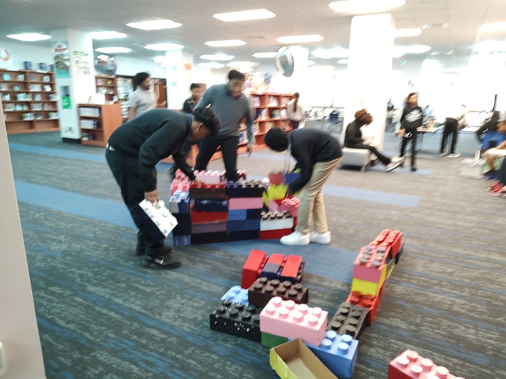 Three students build a house with enlarged cardboard Legos made by art students at Johnson in the library.