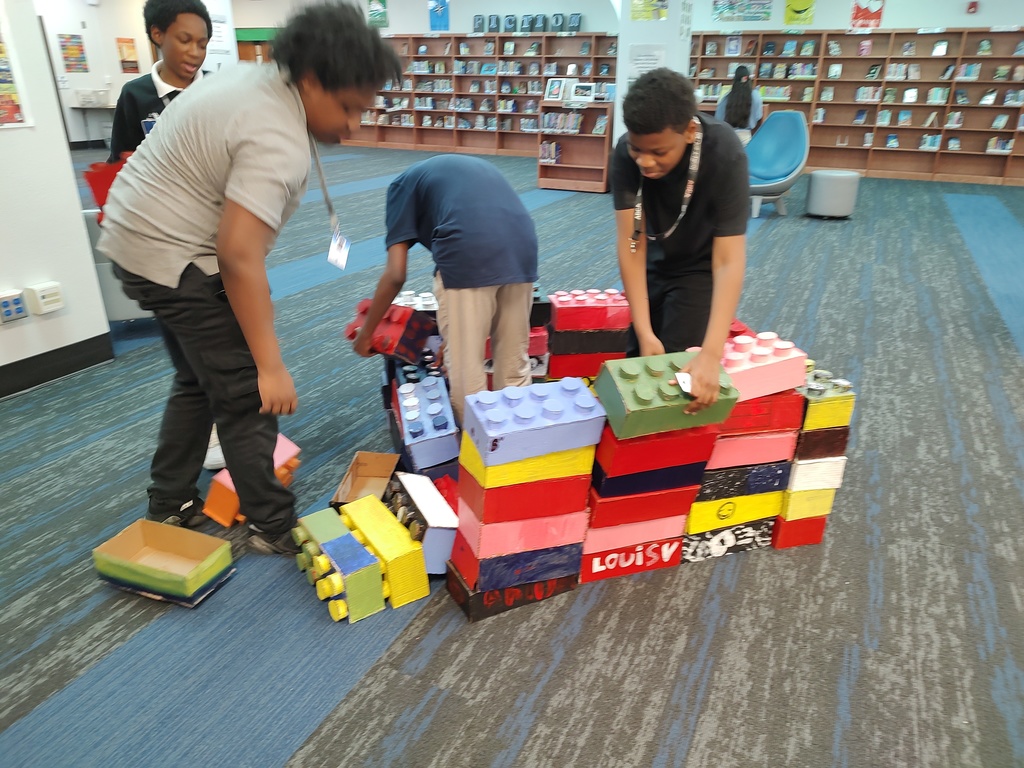 Four students build a house with enlarged cardboard Legos made by art students at Johnson in the library.