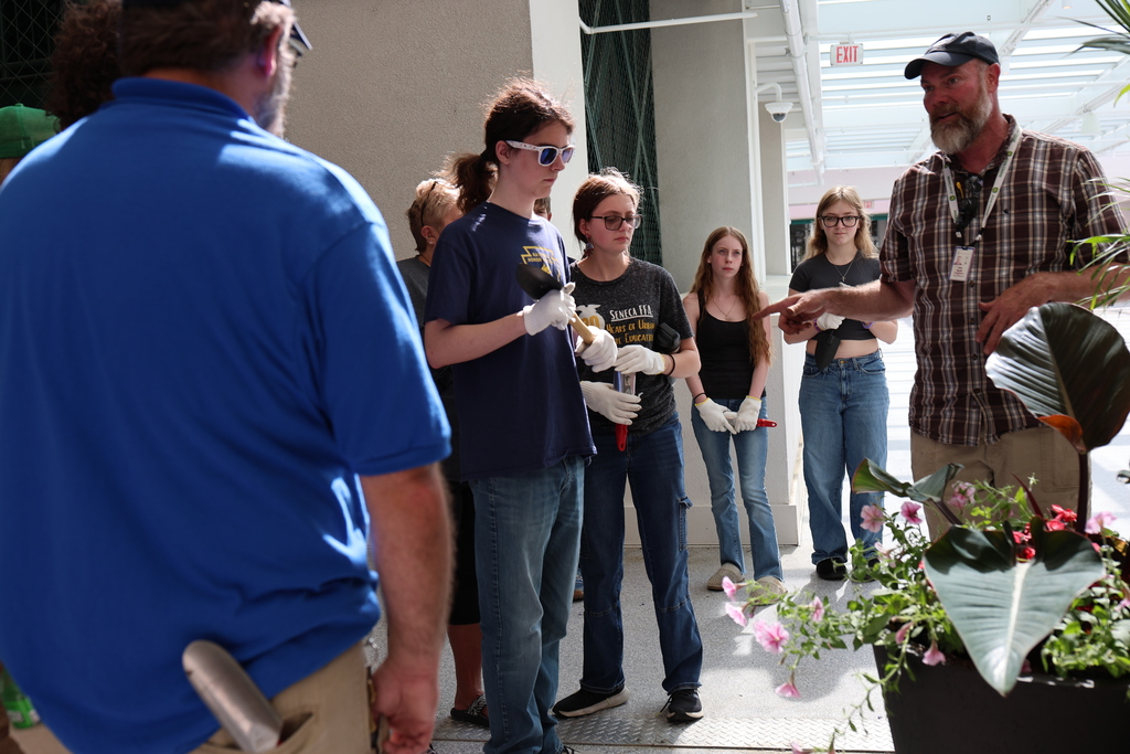 An adult talks to students near a flower pot. 