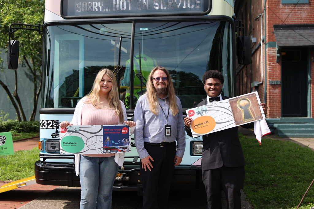 Two students stand with an adult in front of a TARC bus.