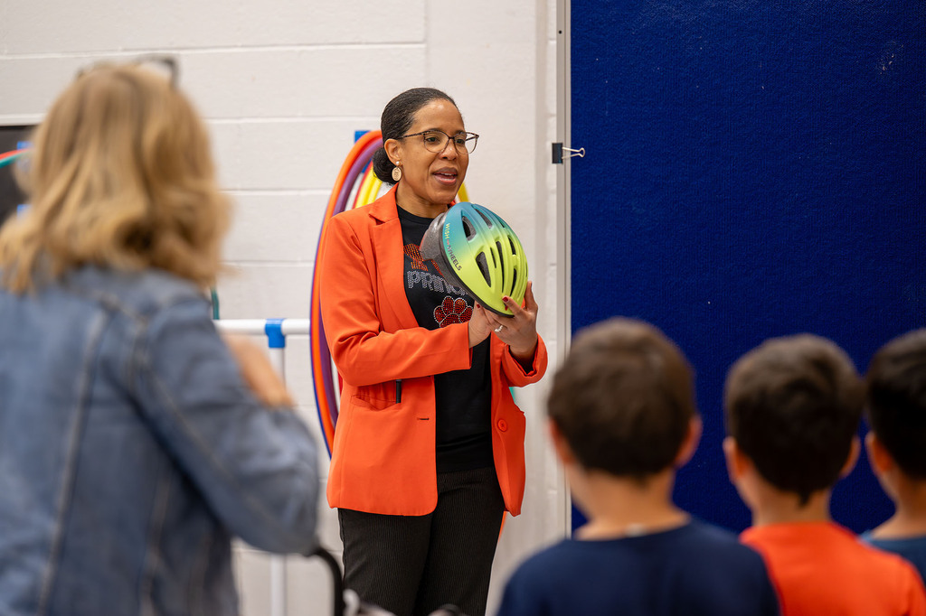 An adult holds up a helmet and shows it to students.