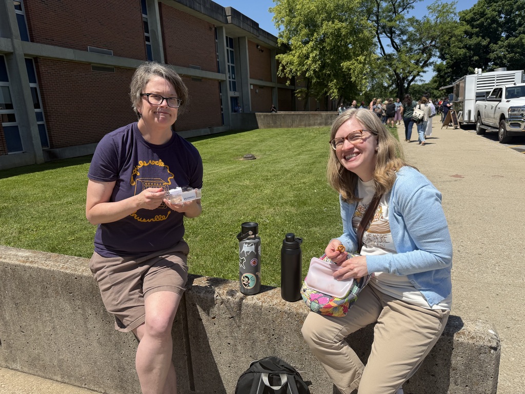 Two adults eat food outside.