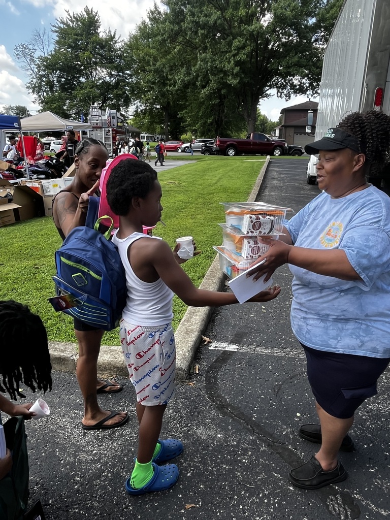 An adult hands a student summer meals.