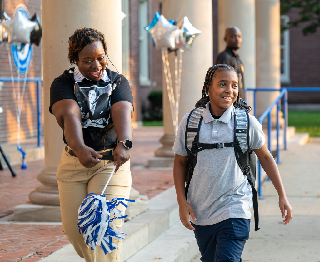 An adult cheers as a student walks into school.