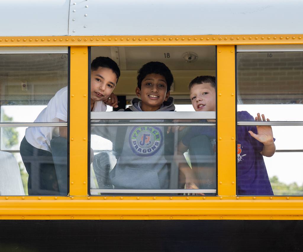 Three students smile out of a bus window.