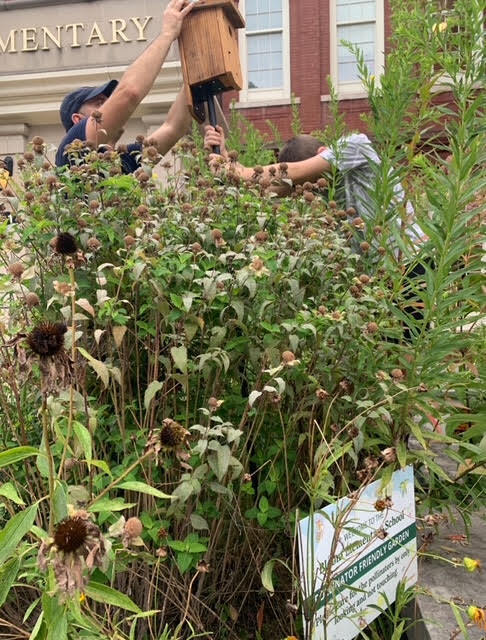 A student and an adult install a bird feeder near Bloom Elementary.