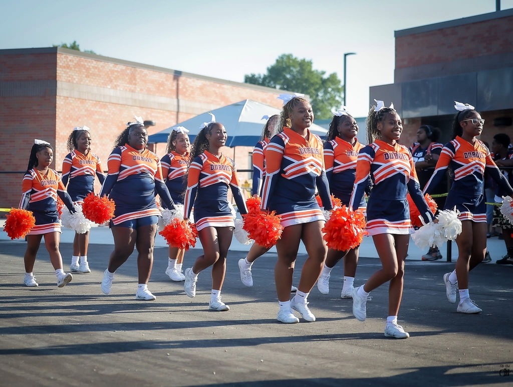 Cheerleaders walk while holding pom poms.