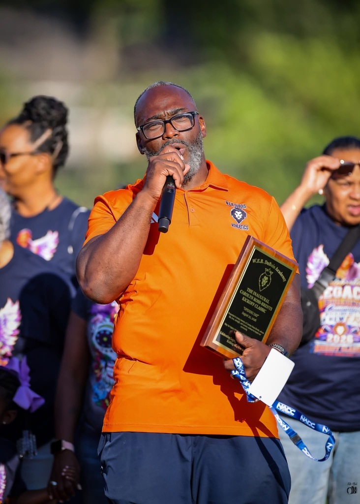 A man hold a plaque and speaks into a microphone.
