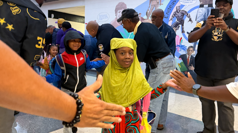 Surprised student high fiving flash dads, with smiling students behind her.