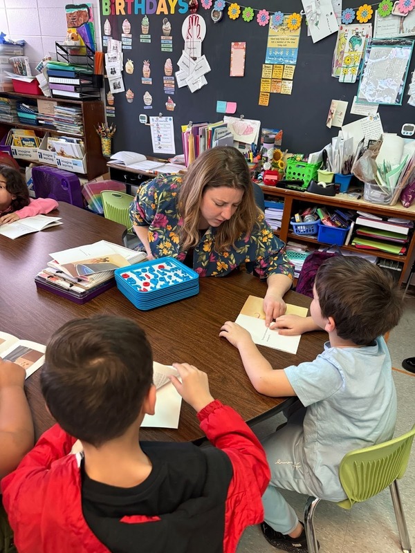 A teacher teachers students at a desk. 