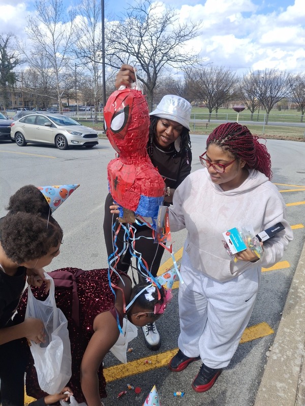 Two adults hold up party supplies while students look on.