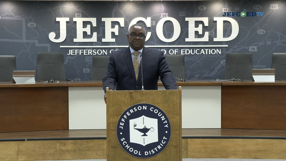 Jefferson County Schools Superintendent Dr. Walter Gonsoulin speaks into a microphone at a podium in the Jefferson County Schools board room.