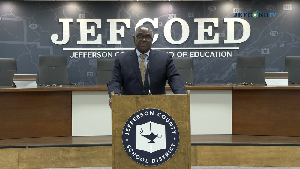 Jefferson County Schools Superintendent Dr. Walter Gonsoulin speaks into a microphone at a podium in the Jefferson County Schools board room.