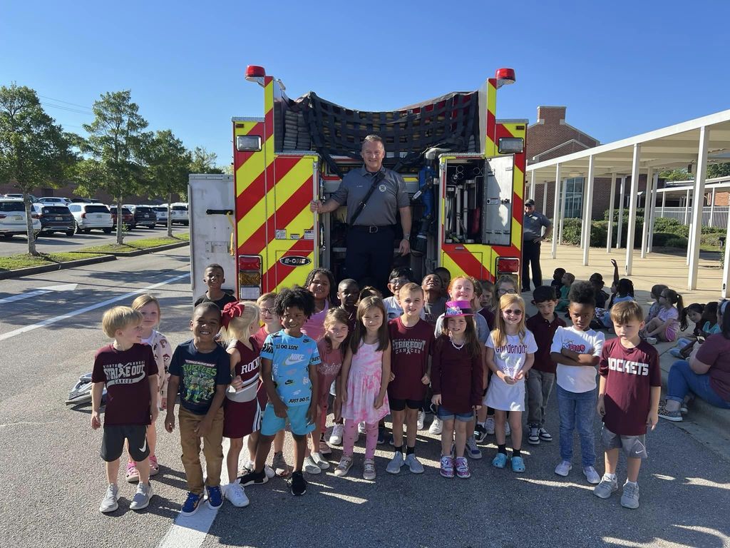 Kindergarten class standing at the back of a firetruck .