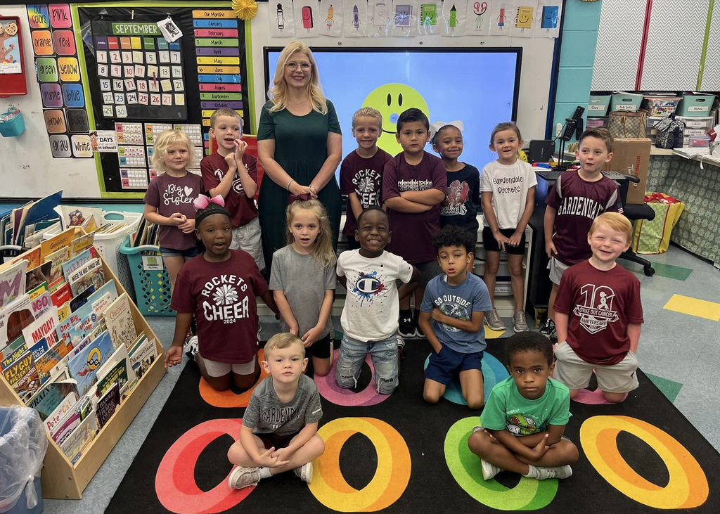 Kindergarten class in classroom on colorful rug.