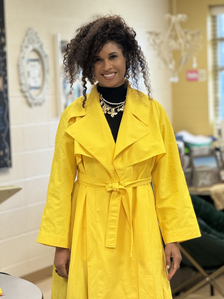 Teacher standing and smiling, wearing a yellow coat