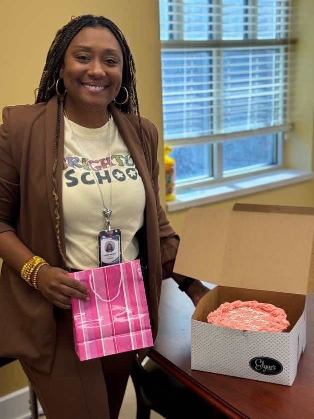 Principal Bryant holding a gift and standing next to a pink cake