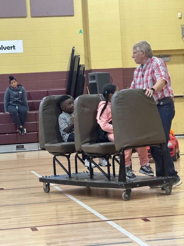 one adult teaching two students how to properly sit in the seats on a school bus