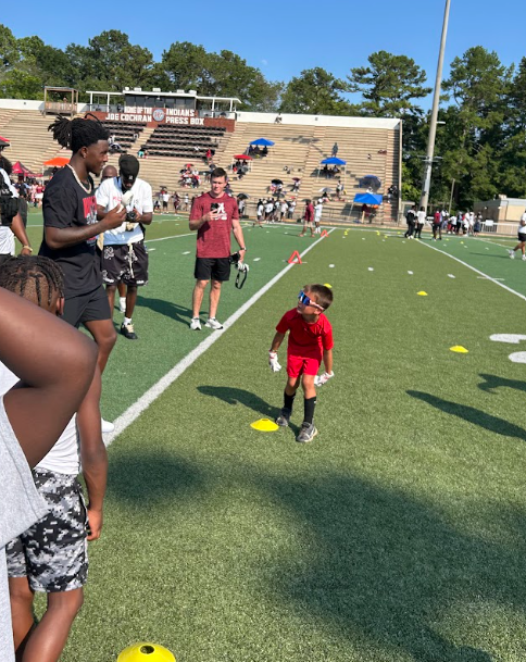 Many people stand in football stadium. In the center of the photo, a young boy looks up at a man who is talking to him.