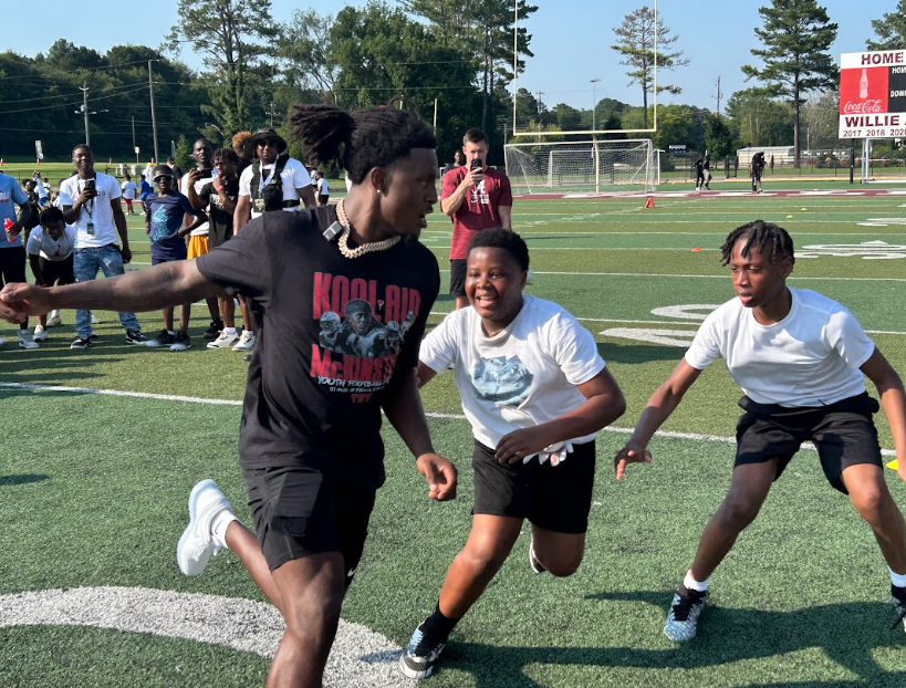 A man runs as two young boys chase after him during a drill on a football field.