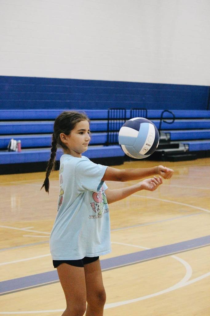 A young girl hits a volleyball against her harm.