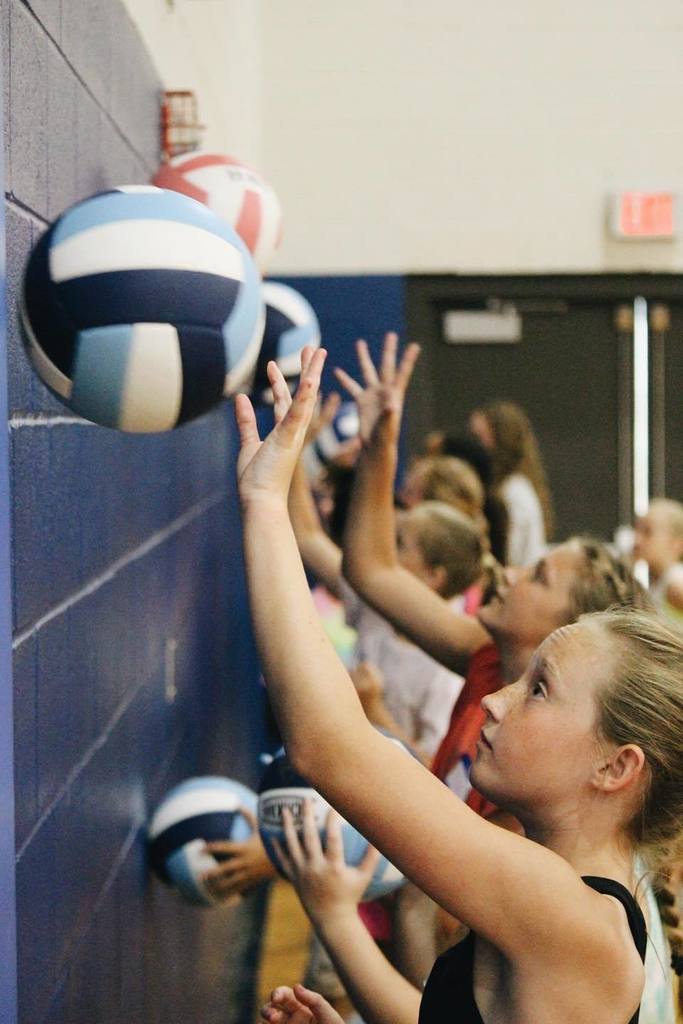 A group of girls hitting volleyballs against a wall