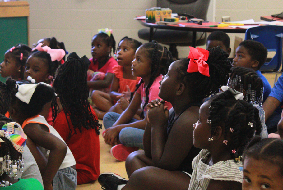 A group of students sit on the floor of a classroom.