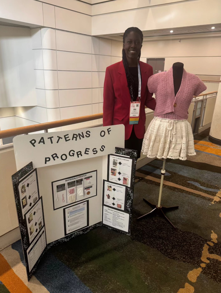 Student stands inside a building, posing next to a poster board and a mannequin