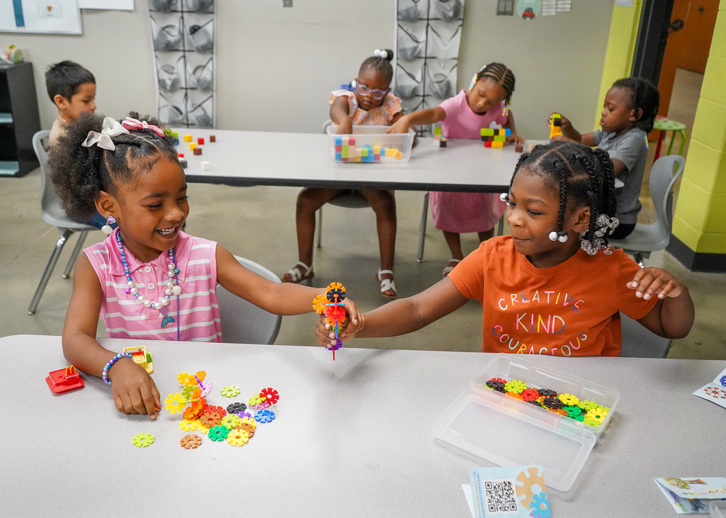 Two students hold plastic flower cutouts while sitting in a classroom.