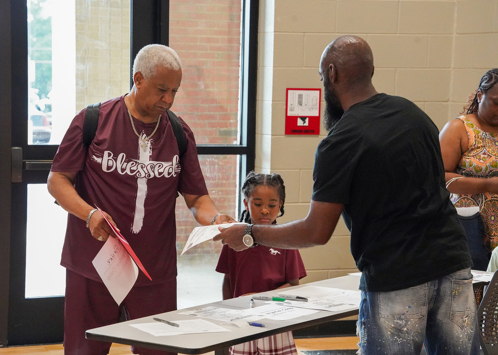 A man hands another man a piece of paper while a child stands nearby